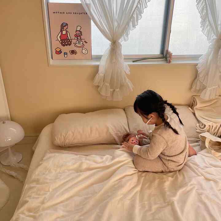 Beige-toned bedroom with a baby playing with a doll on the bed, creating a warm and calm atmosphere