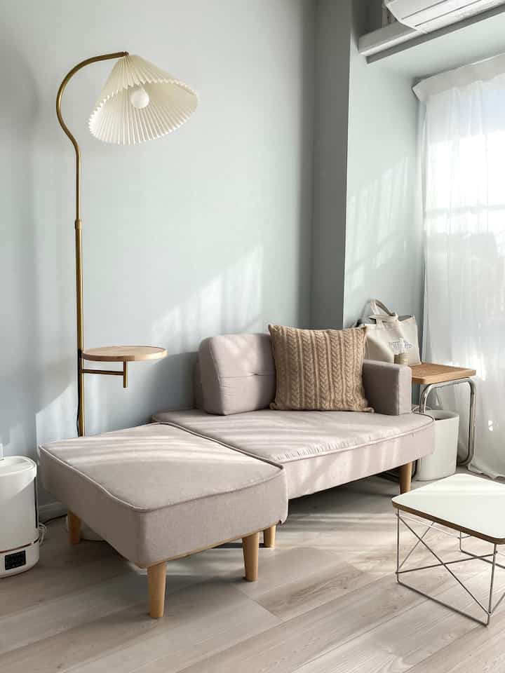 白い壁とベージュのソファが配置されたコンパクトなリビング、自然光とシンプルなレイアウトで広く感じる雰囲気のあるインテリア