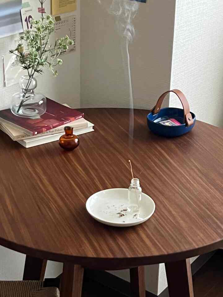 温かみのあるブラウンの木目調ラウンドダイニングテーブル、花瓶と線香が配された落ち着いた一人暮らしの空間