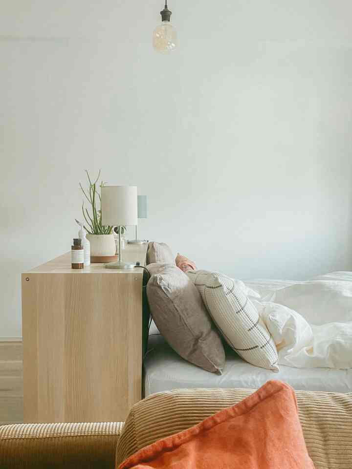 ホワイトとベージュのトーンでまとめられた1LDKの寝室、IKEAの棚の上にテーブルランプとクッションが配置された自然で落ち着く空間