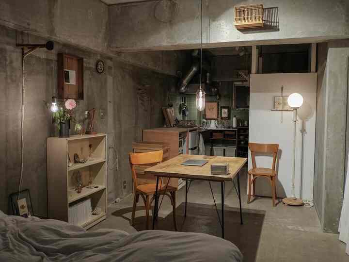 グレー色調のインダストリアルスタイルワンルーム、小型の木目調家具と間接照明が配置された雰囲気のある空間