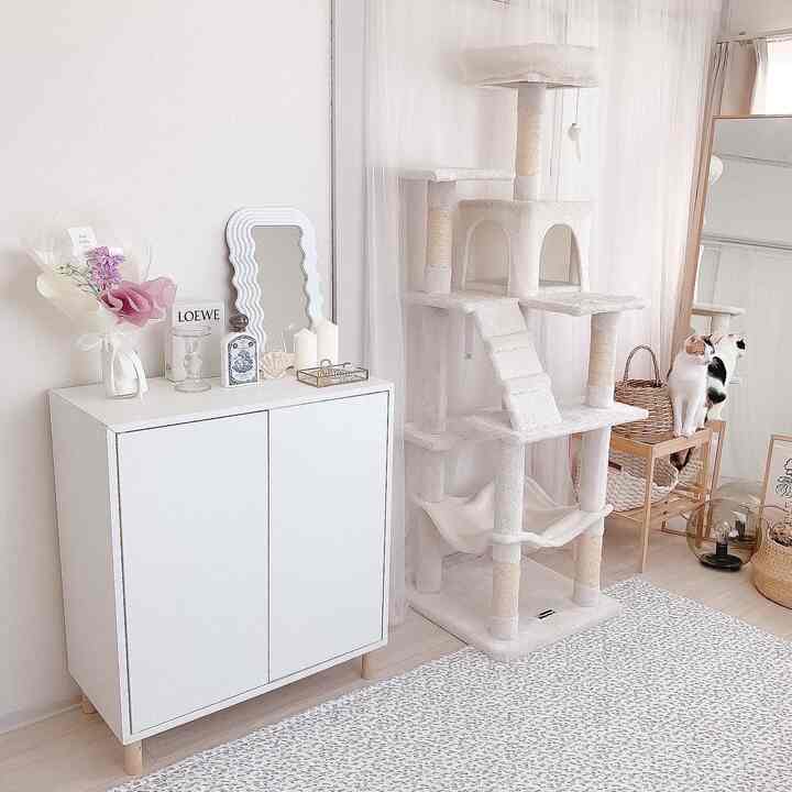 Bright white and beige toned living area featuring a white storage cabinet and a large cat tower with two cats sitting, creating a simple and natural atmosphere