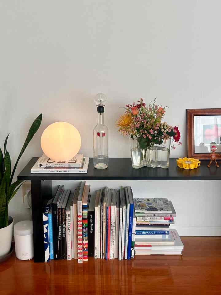 ナチュラルな色調のダイニングの本棚に花瓶とテーブルランプが配置された雰囲気のあるインテリア
