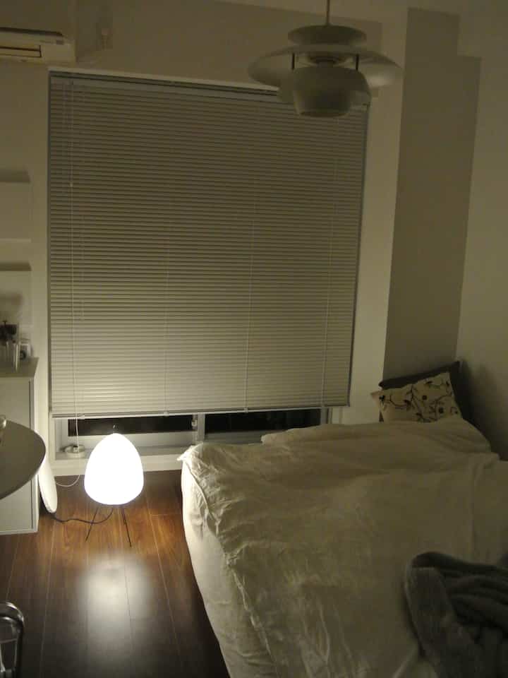White and brown toned bedroom featuring a bed, blinds, and a floor lamp creating a cozy atmosphere