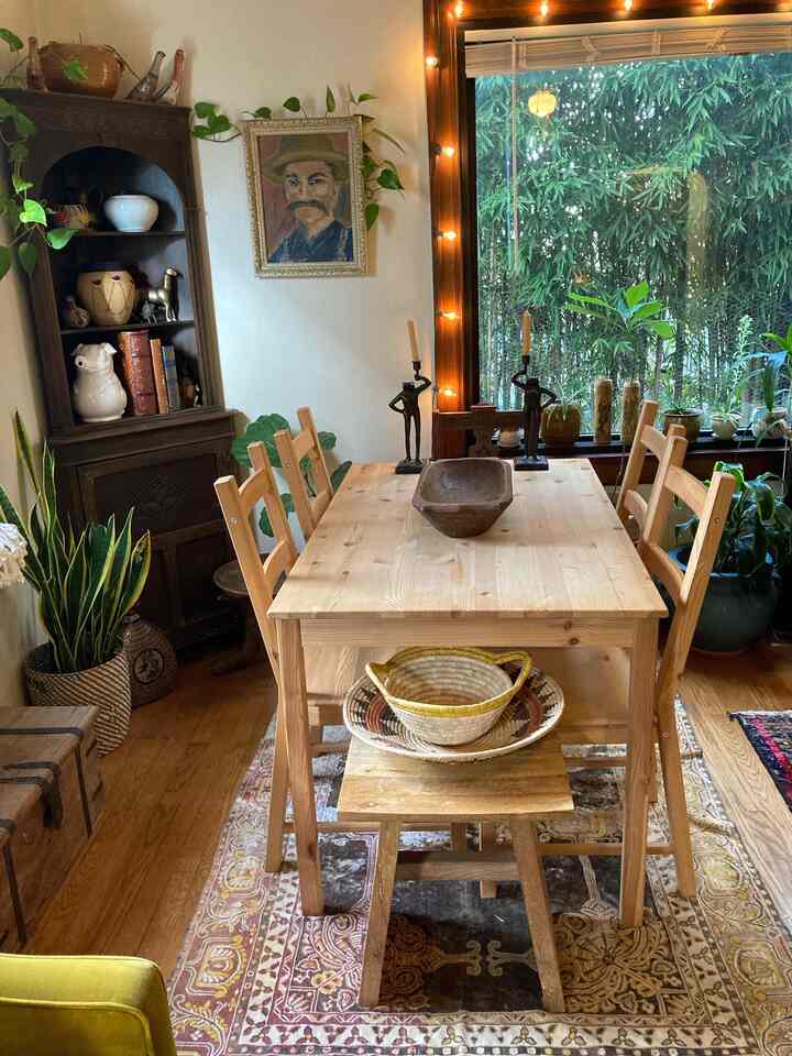 Natural wood-tone dining room featuring a wooden dining table and chairs surrounded by lush plants and a corner storage cabinet, creating a cozy atmosphere