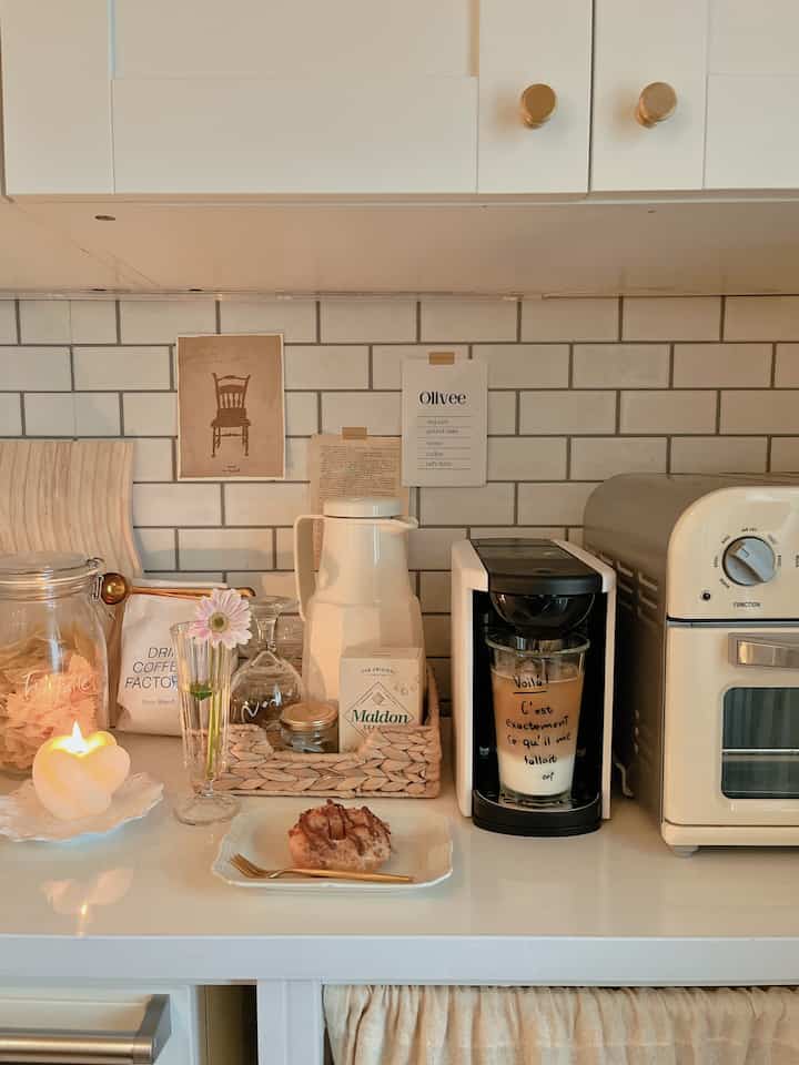 White and beige toned kitchen space featuring candle, coffee maker, and donut creating cozy home cafe vibe