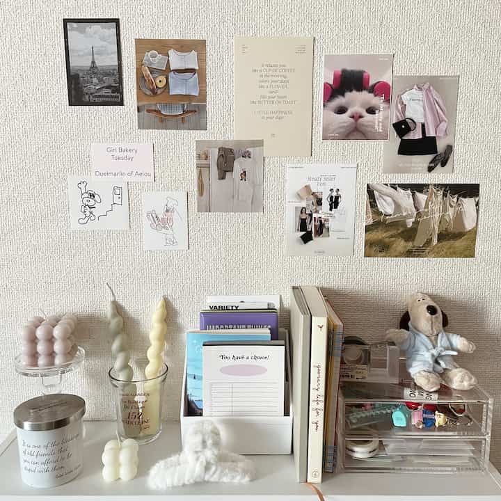 白と透明素材が調和した小さな空間、壁に様々なポスターやカードが飾られ、書籍やキャンドルが整頓された印象的なインテリア。