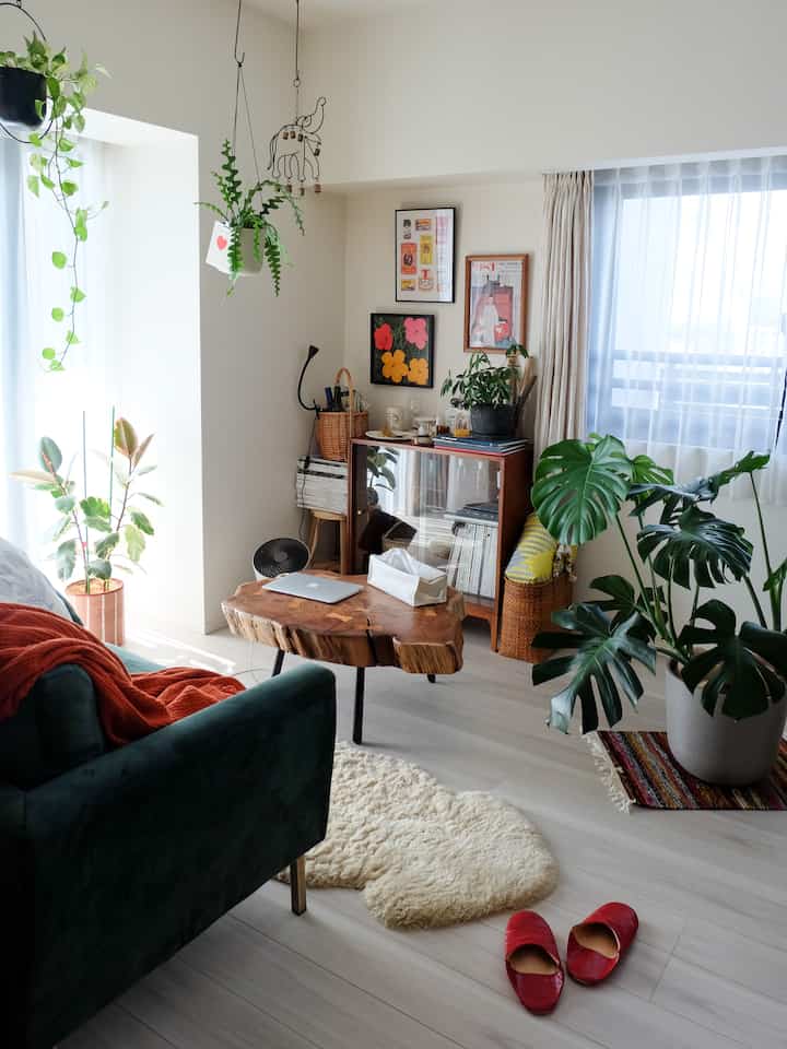 明るく暖かい自然な木目調とグリーン植物が調和したリビング、グリーンのベルベットソファとライブエッジのコーヒーテーブルが配置された雰囲気のあるインテリア