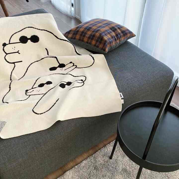 Natural modern living room featuring a gray sofa and black round stool, with a cute dog-patterned blanket draped over the sofa under soft natural light