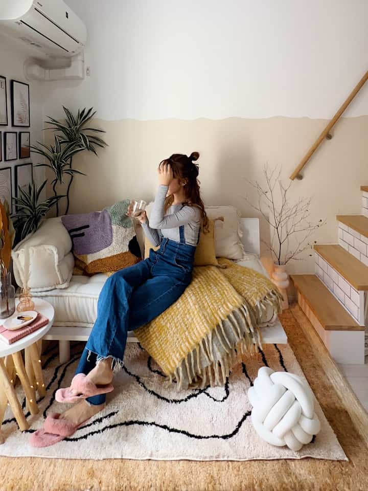 黄色とベージュの色合いのリビング、白いソファとラグ、植物と壁照明が配置された雰囲気のあるインテリア