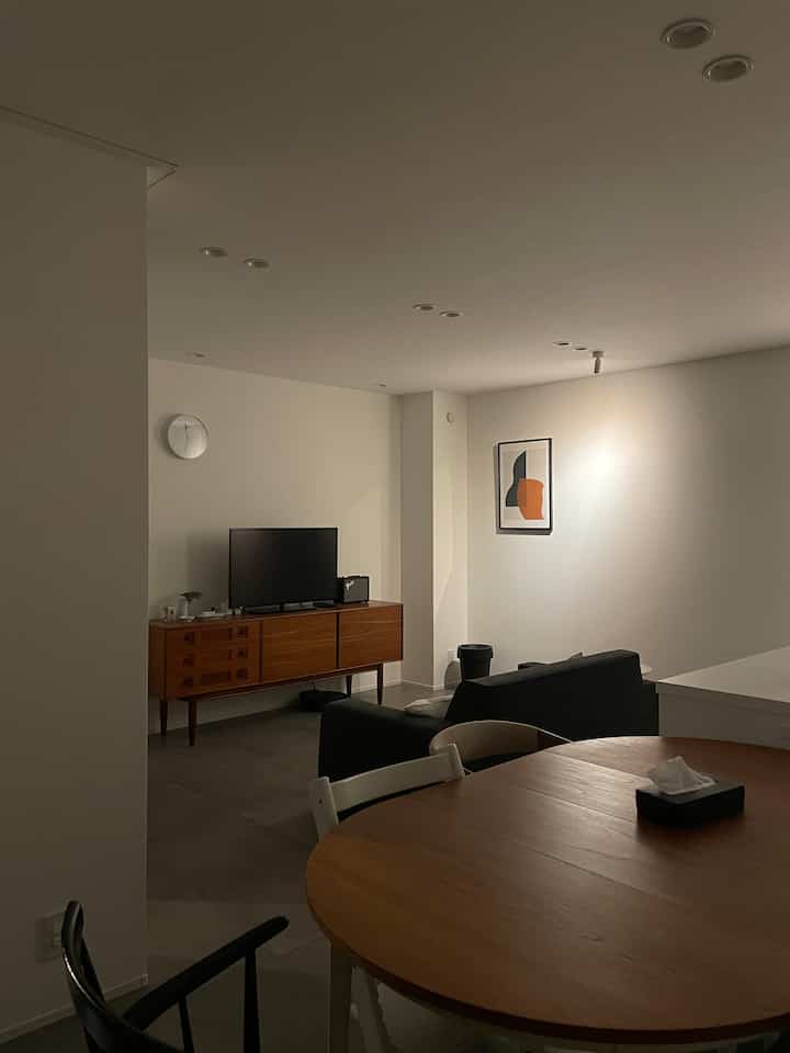 Minimal style living room with white walls, brown wooden dining table, black sofa, and TV stand arranged comfortably