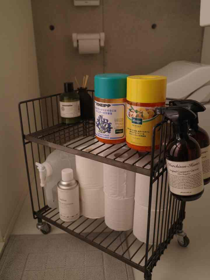 ホワイトとブラックのトーンのバスルーム、ワイヤーワゴンにバス用品とトイレットペーパーが整頓されたコンパクトな空間