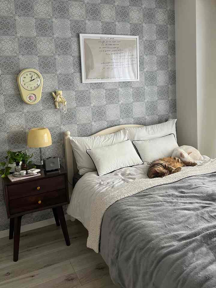 グレーとホワイトのトーンの寝室、ベッドの上に二匹の猫が寝ており、横にテーブルランプとチェストが配置された印象的な空間