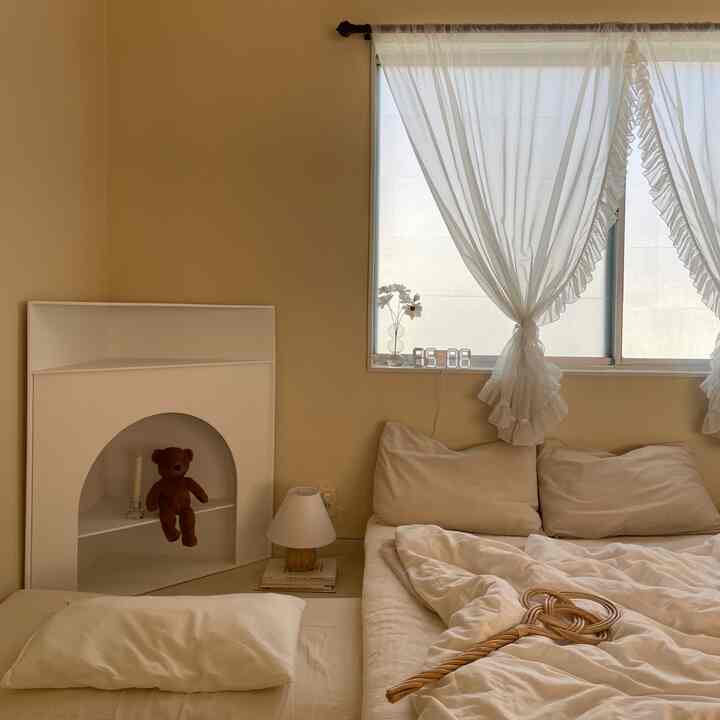 柔らかなベージュとホワイトの色調の寝室、窓際のコーナーマントルピースと快適な寝具が配置されたナチュラルなインテリア