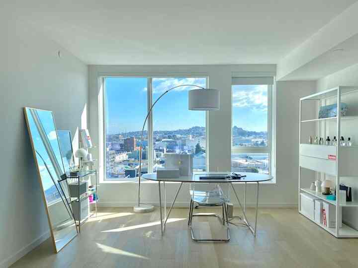 Bright white and natural tone home office space featuring large windows and a transparent chair in a minimalist setting