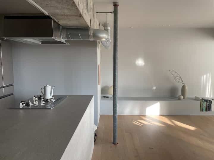 ナチュラルカラーとグレーのトーンが調和するキッチンスペース、シンプルな家具とスチール柱が特徴のモダンなインテリア