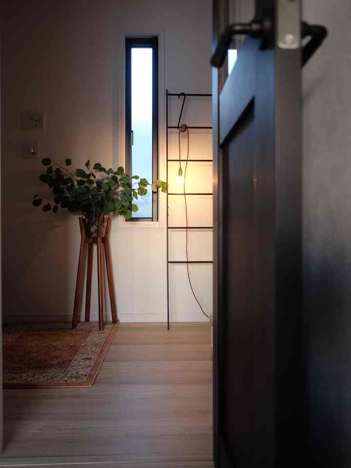 白い壁と木目調の床のミニマルな玄関、ペンダントライトと観葉植物が配置された雰囲気のある空間