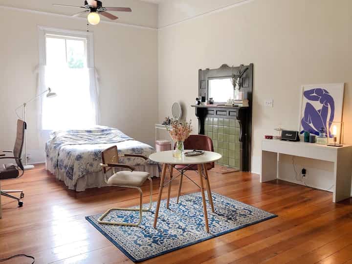 Bright white-toned bedroom with wood flooring, medium bed, round table, featuring a cozy Mid-Century Modern style