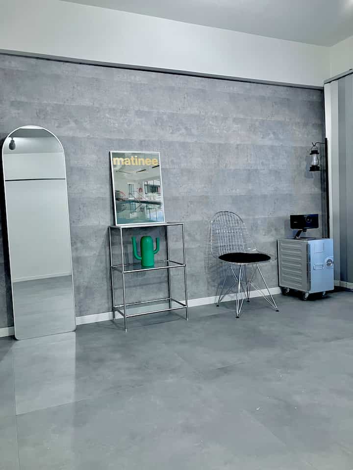 グレーのトーンのリビング、スチールの棚と金属製チェア、大型のスタンドミラーがシンプルに配置された空間