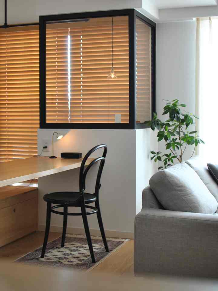 Natural tone living room with a gray sofa, black chair, wooden blinds, and a plant in a modern setup
