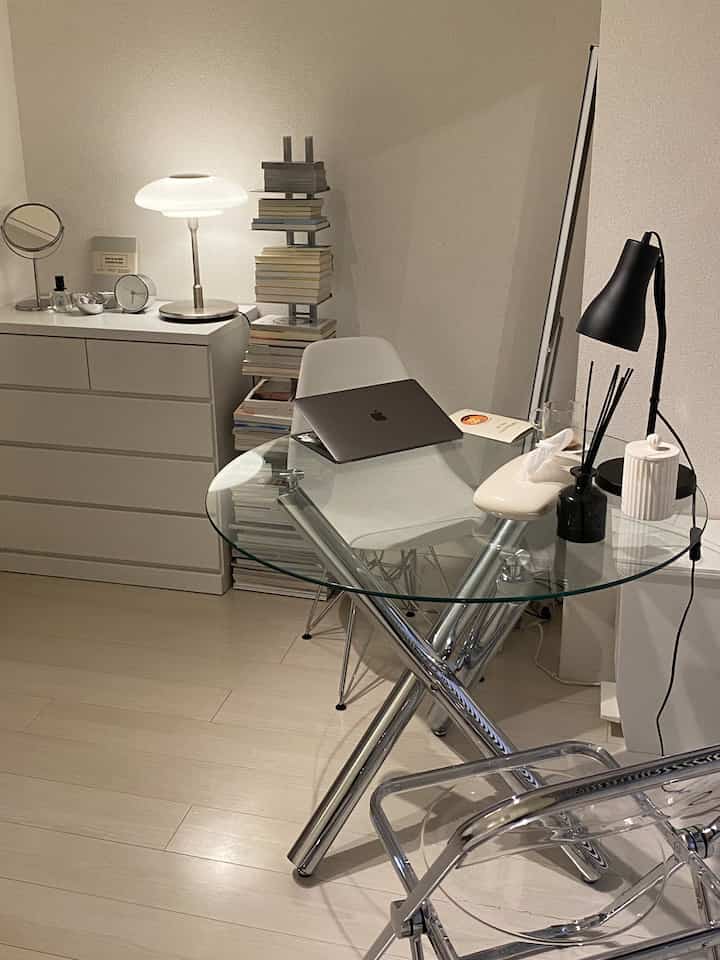 ホワイトとシルバーの色調でまとめられたコンパクトなホームオフィス、ガラスデスクと本棚、テーブルランプが配置された清潔感のあるインテリア