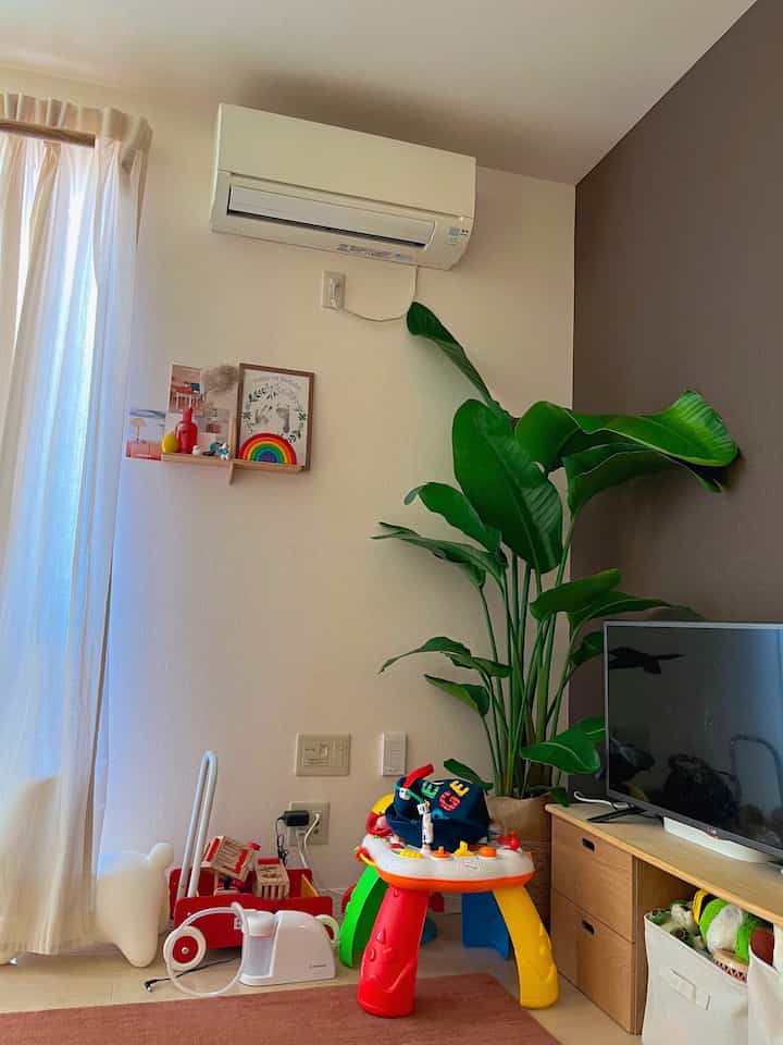 ベージュの落ち着いたリビング、大きな緑の植物と子供のおもちゃがある雰囲気のある空間