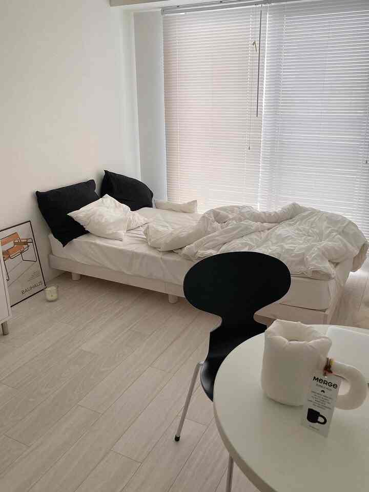 白と黒の調和が取れたワンルーム寝室、ミニマルな家具と明るい木目調の床が落ち着いた雰囲気を演出