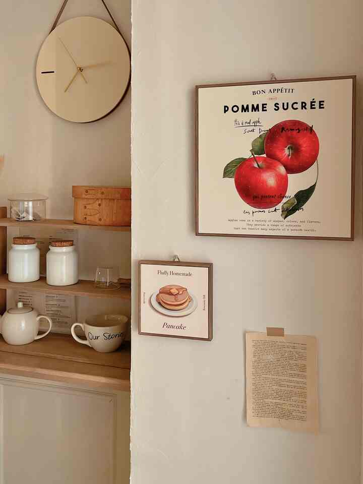 ベージュと木目調のキッチン壁、リンゴのポスターとパンケーキの絵が配された雰囲気のあるカフェ風インテリア