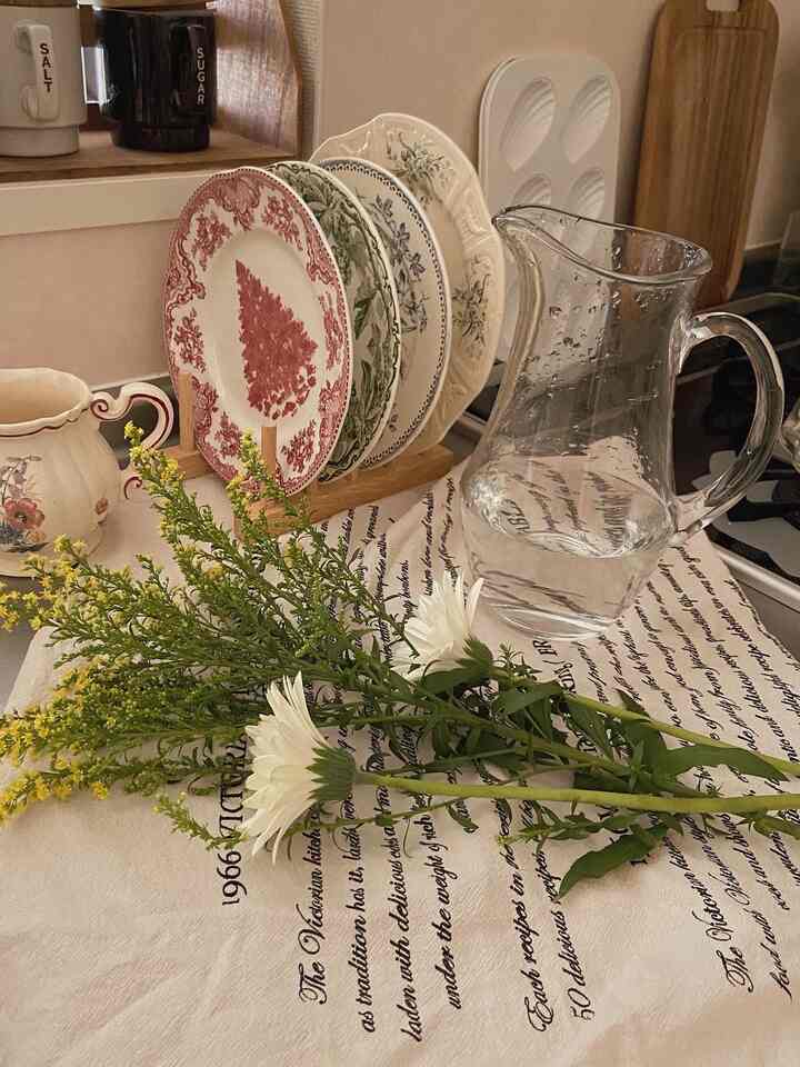 White and green toned kitchen featuring a vase with flowers, vintage plates, and a table runner with cozy atmosphere