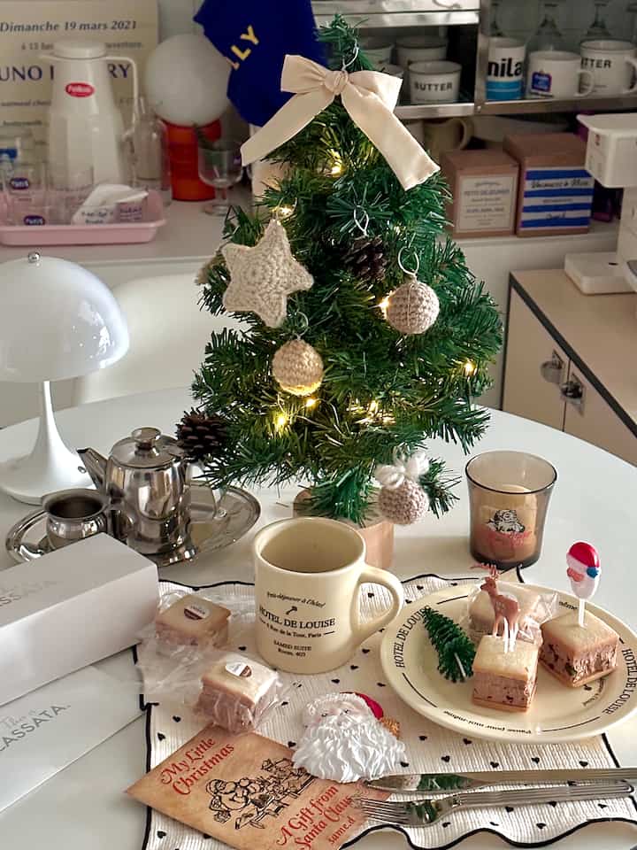 ホワイトトーンの小さなダイニングルーム、ミニクリスマスツリーとコーヒーマグが配置された雰囲気のあるおうちカフェ空間