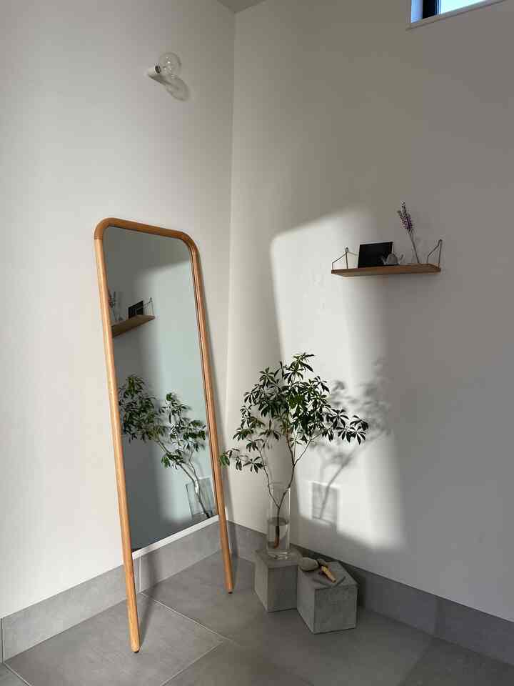 白と木目調の玄関、大きな木製鏡と植物が配置されたミニマルで自然な雰囲気のあるインテリア