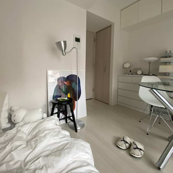 Natural tone single room featuring simple furniture with bed, desk, and stool arranged in a cozy space