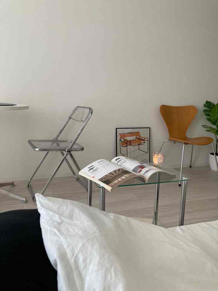 A calm monotone living room featuring steel and transparent materials with a glass side table and designer chairs arranged simply