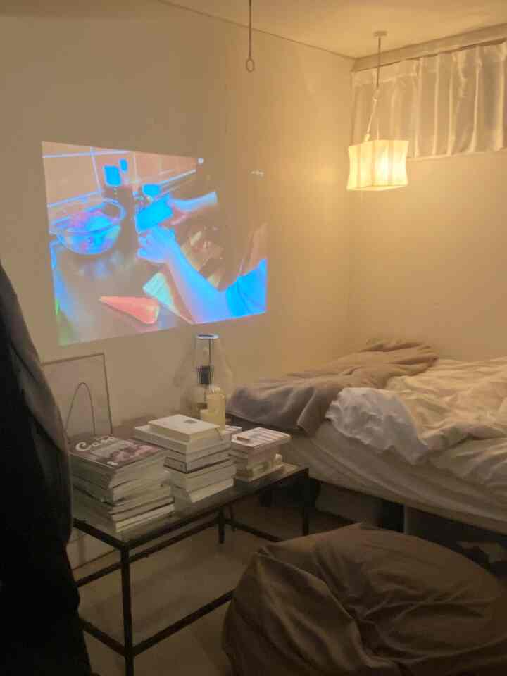 ベージュ色調のコンパクトなワンルームリビング、ベッドとビーズクッションが配置された居心地の良いホームシネマと読書空間