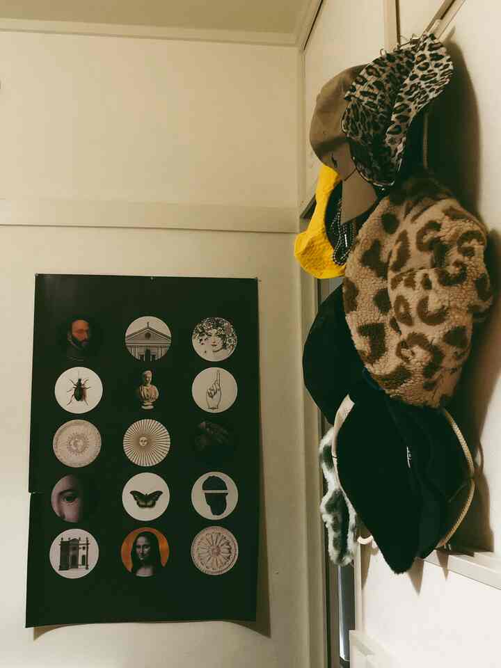 ベージュ色の壁に黒い歴史ポスターが掛かり、右側の壁には様々な帽子が掛けられた雰囲気のある玄関スペース