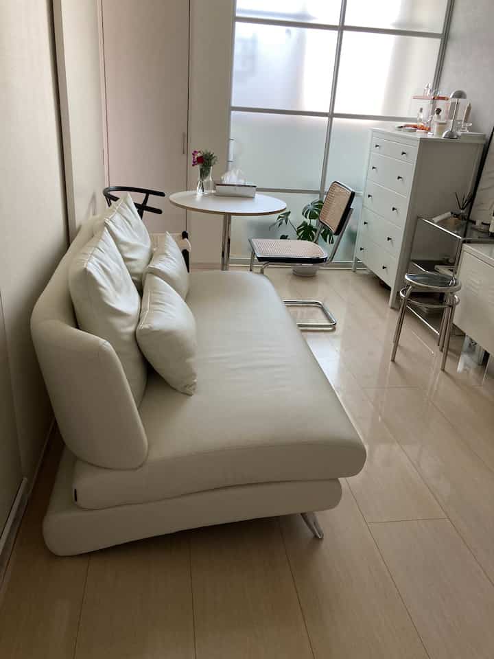 White and wood-tone long narrow living room featuring sofa, dresser, stool in a clean minimalist layout