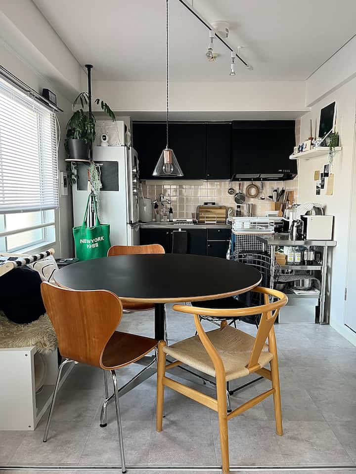 A modern 1LDK kitchen and dining room in white and black tones featuring wooden chairs and pendant light with a cozy atmosphere