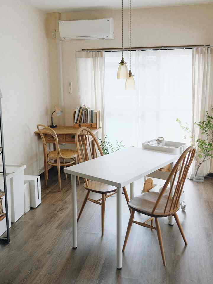 明るい木目調と白を基調とした1LDKのリビング、ダイニングテーブルやチェア、デスク、植物が配置された雰囲気のある空間