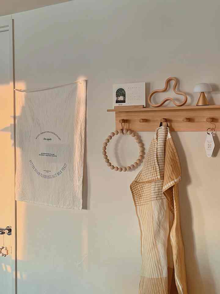 温かみのあるアイボリー色の玄関空間、木製コートハンガーとカレンダー、テキスタイル小物が配置されたシンプルでナチュラルな雰囲気のインテリア