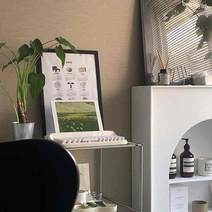 ベージュの壁紙と緑の植物が調和するリビング、キーボードとタブレットを配置したミニマルなホームオフィス空間