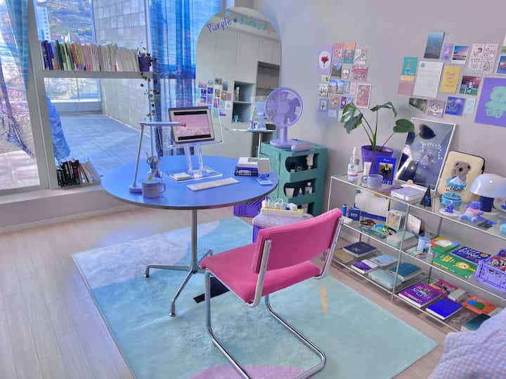 Pastel blue and purple toned home office with round desk and pink chair, bright room illuminated through large window