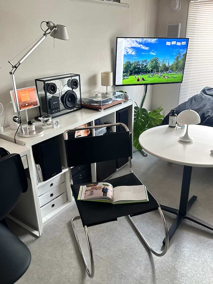White and black toned living room featuring a black chair, round table with table lamp, bookshelf, and audio equipment in a neat interior