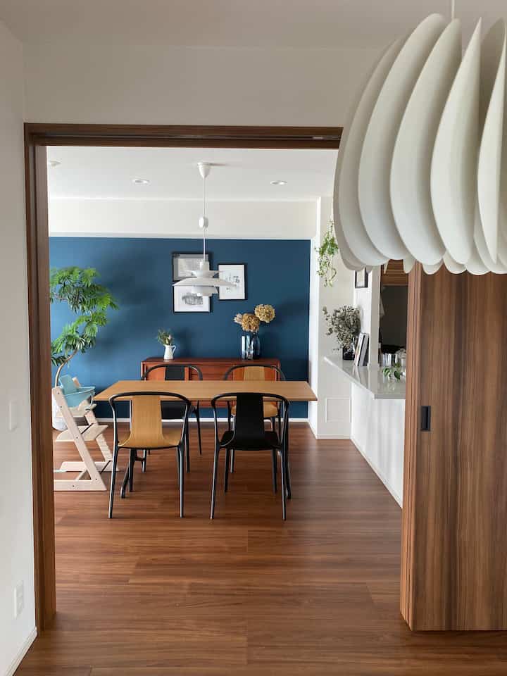 ナチュラルな木目調と青いアクセントウォールが際立つ4人掛けダイニング、子供用ハイチェアを備えた温かみのあるリビング空間