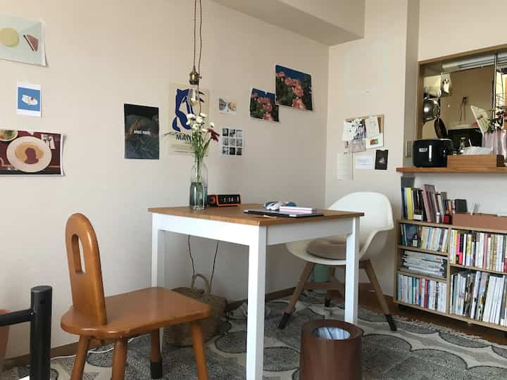 明るいベージュの壁と白いテーブルがあるナチュラルなダイニング、木製の椅子とペンダントライトが配置された雰囲気のある空間