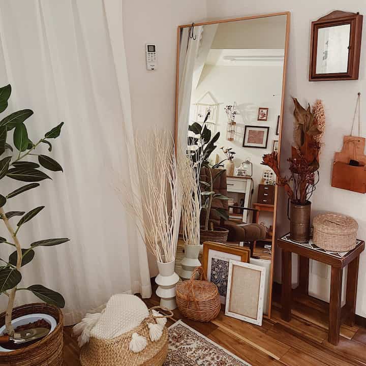 Natural tone living room featuring a large full-length mirror, indoor plants, and wicker baskets creating a cozy warm atmosphere