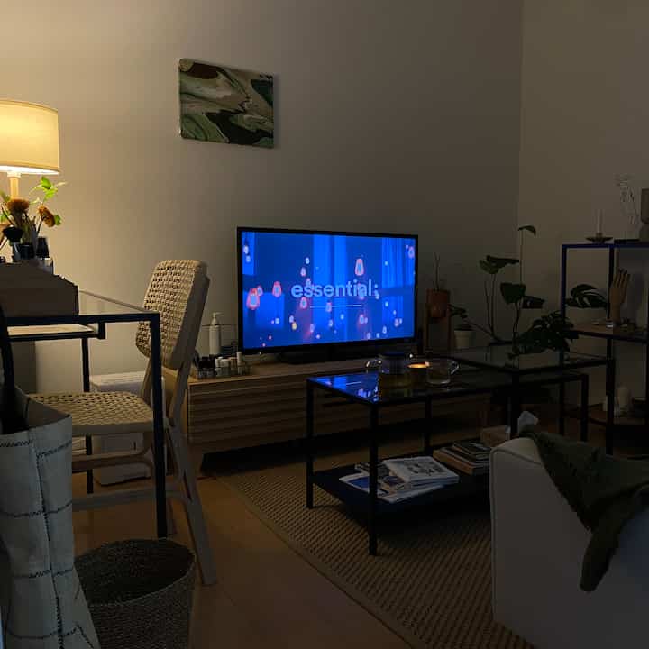 落ち着いた照明とナチュラルカラーのリビング、中央にテレビとソファ、ガラスのコーヒーテーブルが配置されたシンプルな空間