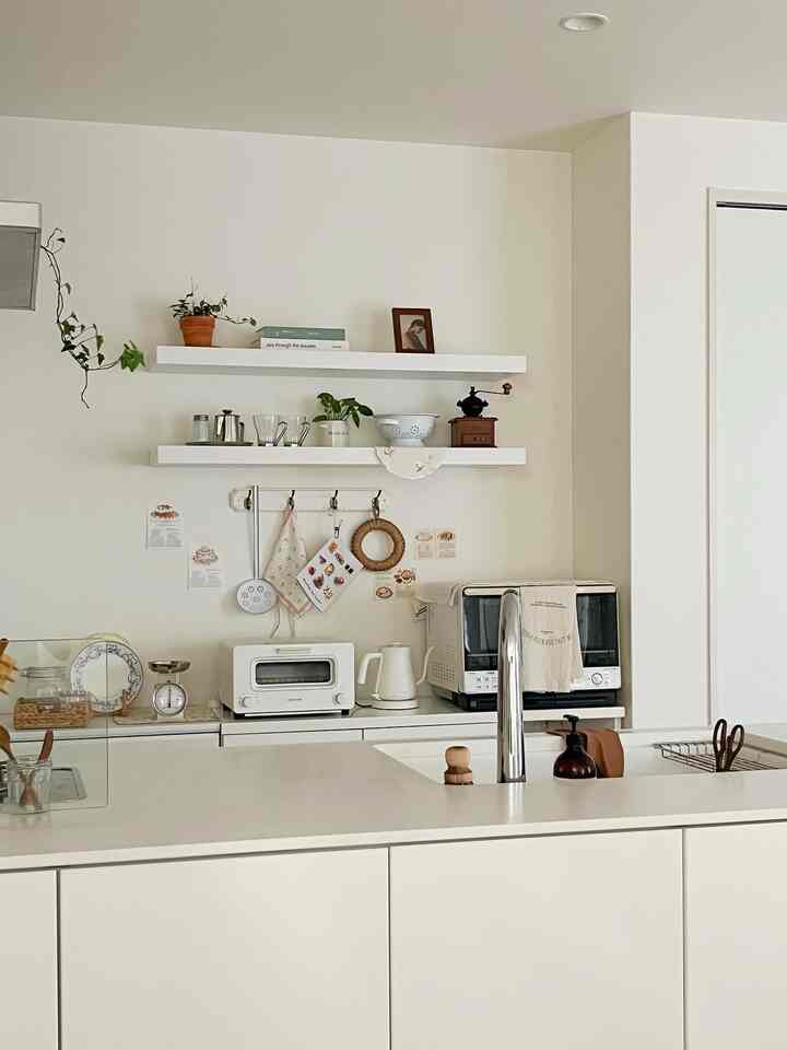 白とナチュラルなトーンの清潔感あるキッチン、壁面に棚や調理器具が配置された雰囲気のある空間