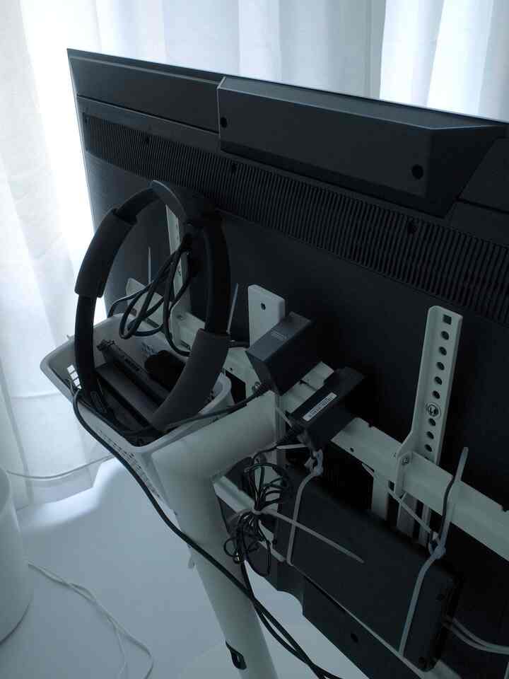 黒いテレビと白いWALLA2スタンドの背面に、結束バンドとバスケットで整理されたニンテンドースイッチや記録装置が見えるリビングルーム