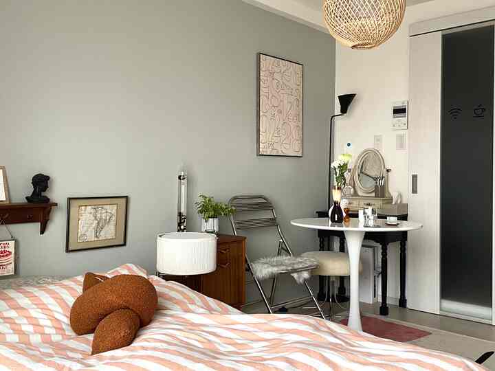 明るいグレーの壁とホワイトの家具が配置された、モダンでナチュラルなワンルームのカフェ風寝室の雰囲気のあるインテリア