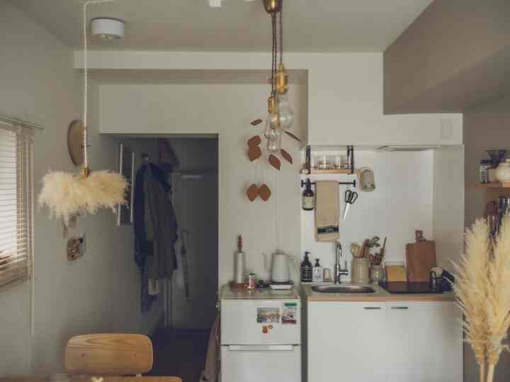 ベージュと白を基調としたワンルームのキッチン、木製ダイニングチェアとエジソンペンダントライトが配置された自然な雰囲気のインテリア